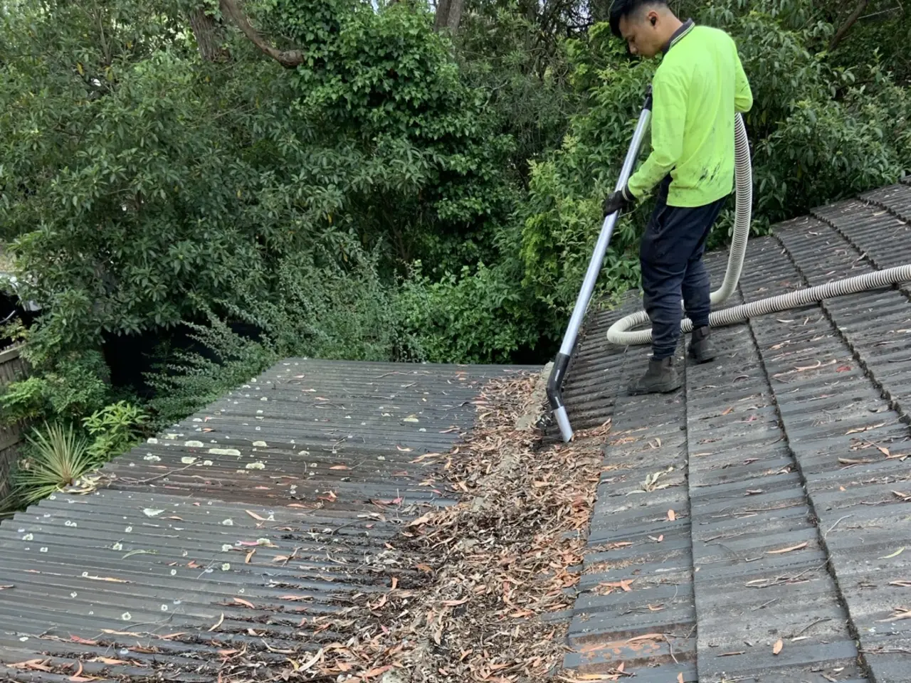 Roofer vacuum cleaning leaves and debris from a tiled roof valley in Melbourne
