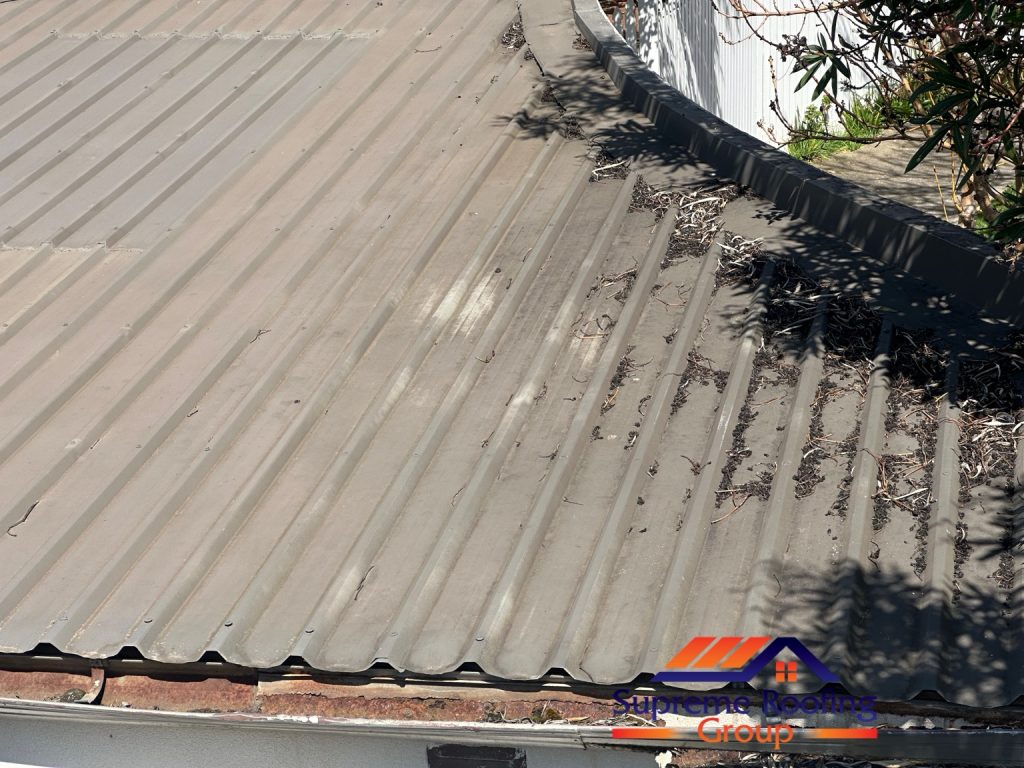 Leaves and debris on metal roof sheets beside rusted guttering before the Toorak repairs